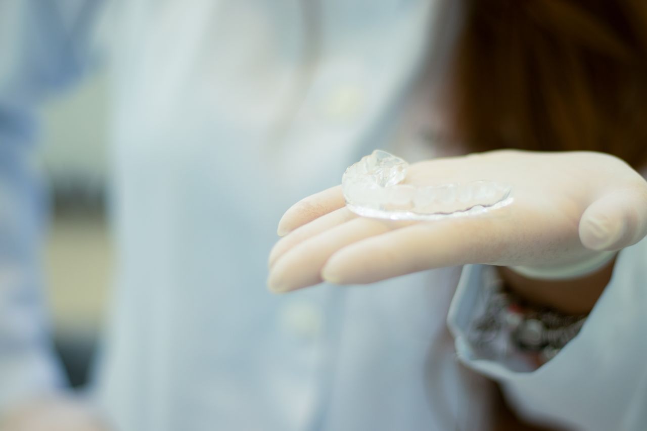 Dentist's gloved hand presenting a transparent mouthguard in a clinical setting.