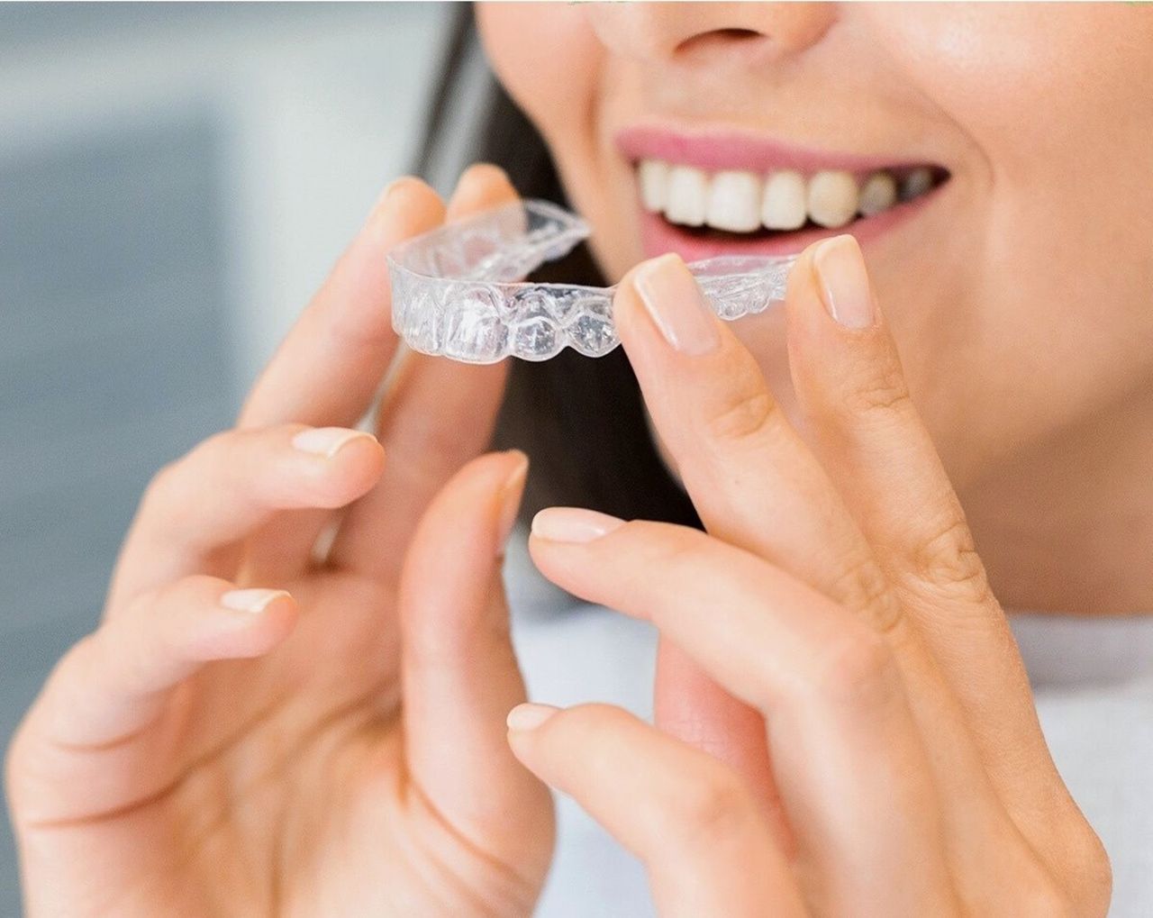 w czym moge pomoc Close-up of a woman holding a clear dental aligner, showcasing dental health and a bright smile.